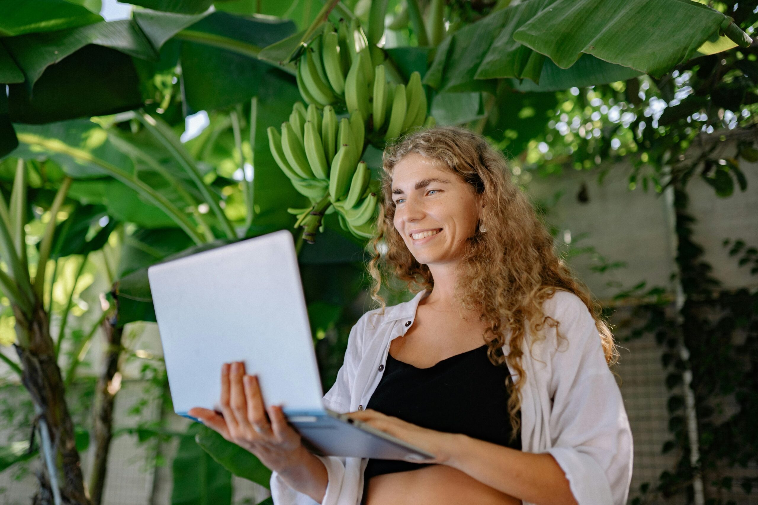 Frau arbeitet nachhaltig mit Laptop unter Bananenstaude - digitale Nachhaltigkeit im Einklang mit der Natur