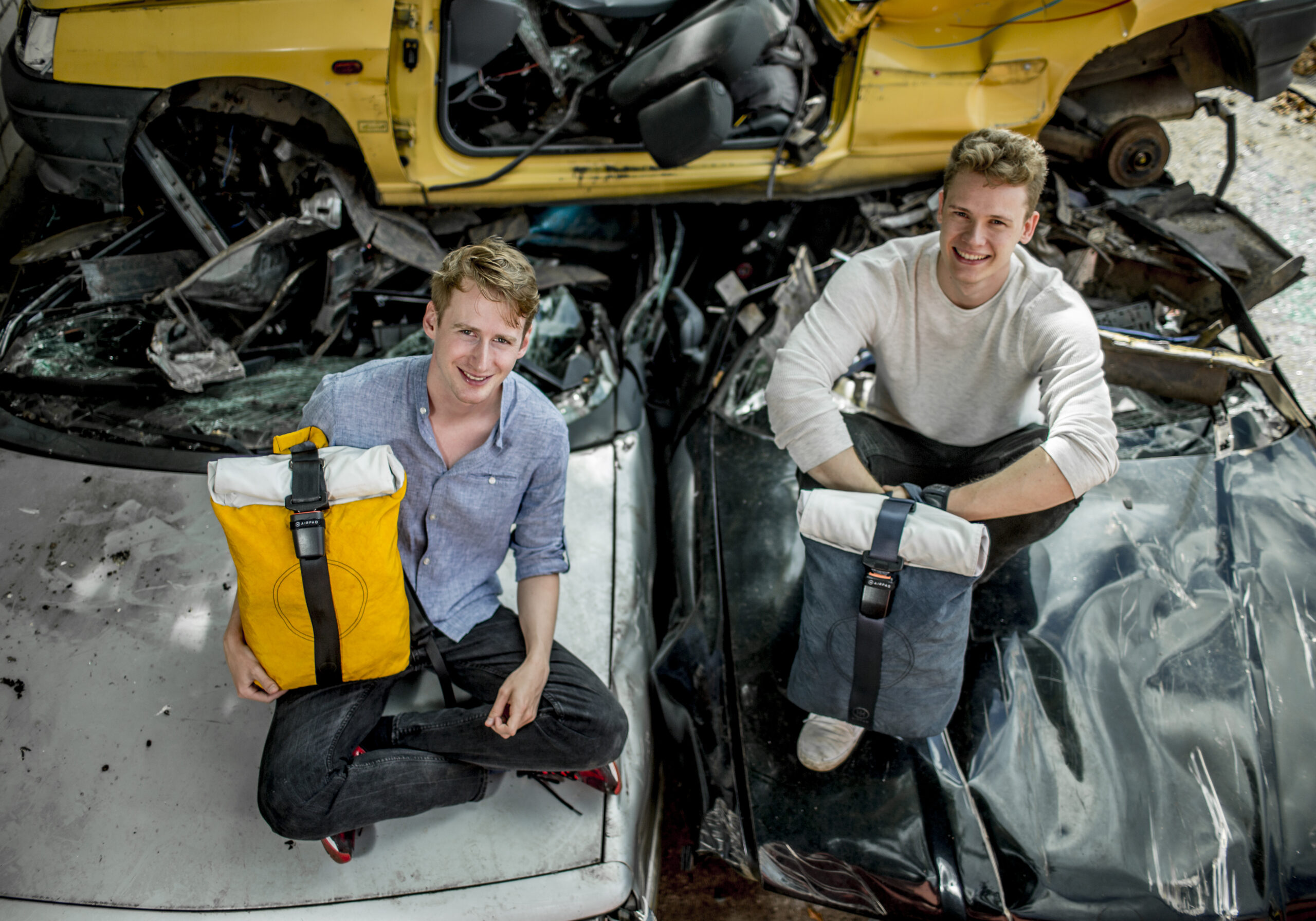 Airpaq-Gründer Adrian Goosses und Michael Widmann mit nachhaltigen Rucksäcken aus upgecycelten Autoteilen vor Autoschrottplatz - Green Fashion Start-Up aus Köln