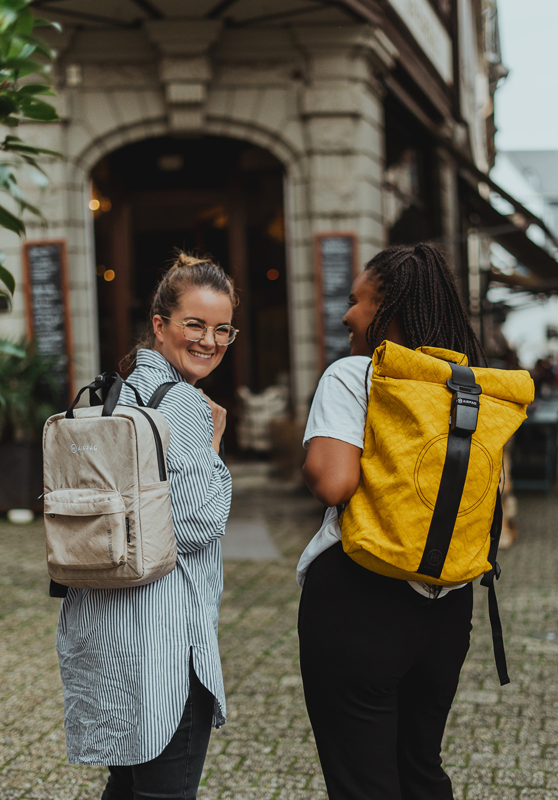 Zwei junge Frauen mit Airpaq Rucksäcken in beige und gelb - Stylische nachhaltige Upcycling-Taschen aus upgecycelten Materialien für urbanen Lifestyle