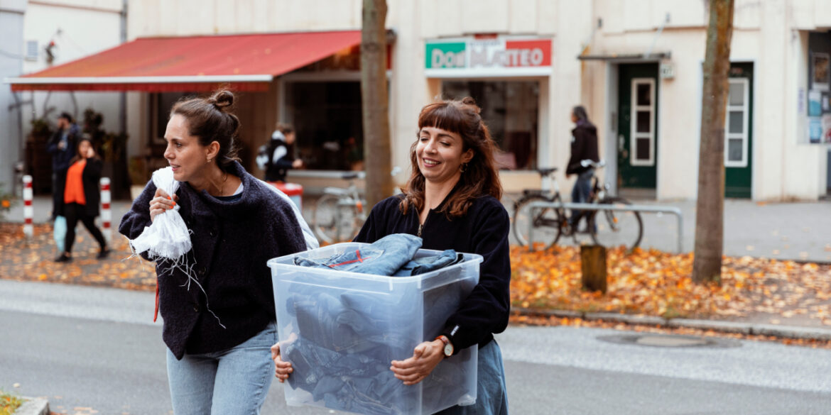 Vielfältiges Produktionsteam der Bridge&Tunnel GmbH Hamburg bei der nachhaltigen Upcycling-Arbeit mit Jeansstoffen in der Textilmanufaktur. Drei Mitarbeiterinnen mit unterschiedlichen kulturellen Hintergründen schneiden und verarbeiten Denim-Materialien zu neuen Designerstücken - ein anschauliches Beispiel für soziale Integration und nachhaltige Modewirtschaft.