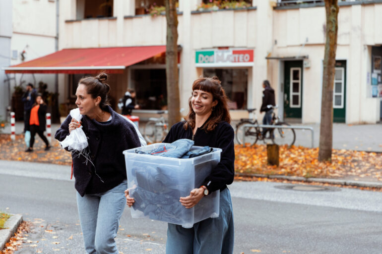 Vielfältiges Produktionsteam der Bridge&Tunnel GmbH Hamburg bei der nachhaltigen Upcycling-Arbeit mit Jeansstoffen in der Textilmanufaktur. Drei Mitarbeiterinnen mit unterschiedlichen kulturellen Hintergründen schneiden und verarbeiten Denim-Materialien zu neuen Designerstücken - ein anschauliches Beispiel für soziale Integration und nachhaltige Modewirtschaft.